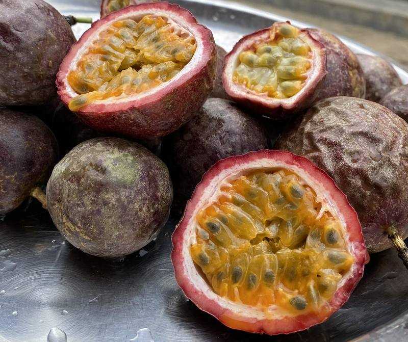 Ripe purple passion fruit, whole and cut open to show the pulp and seeds: the fruit these plants produce